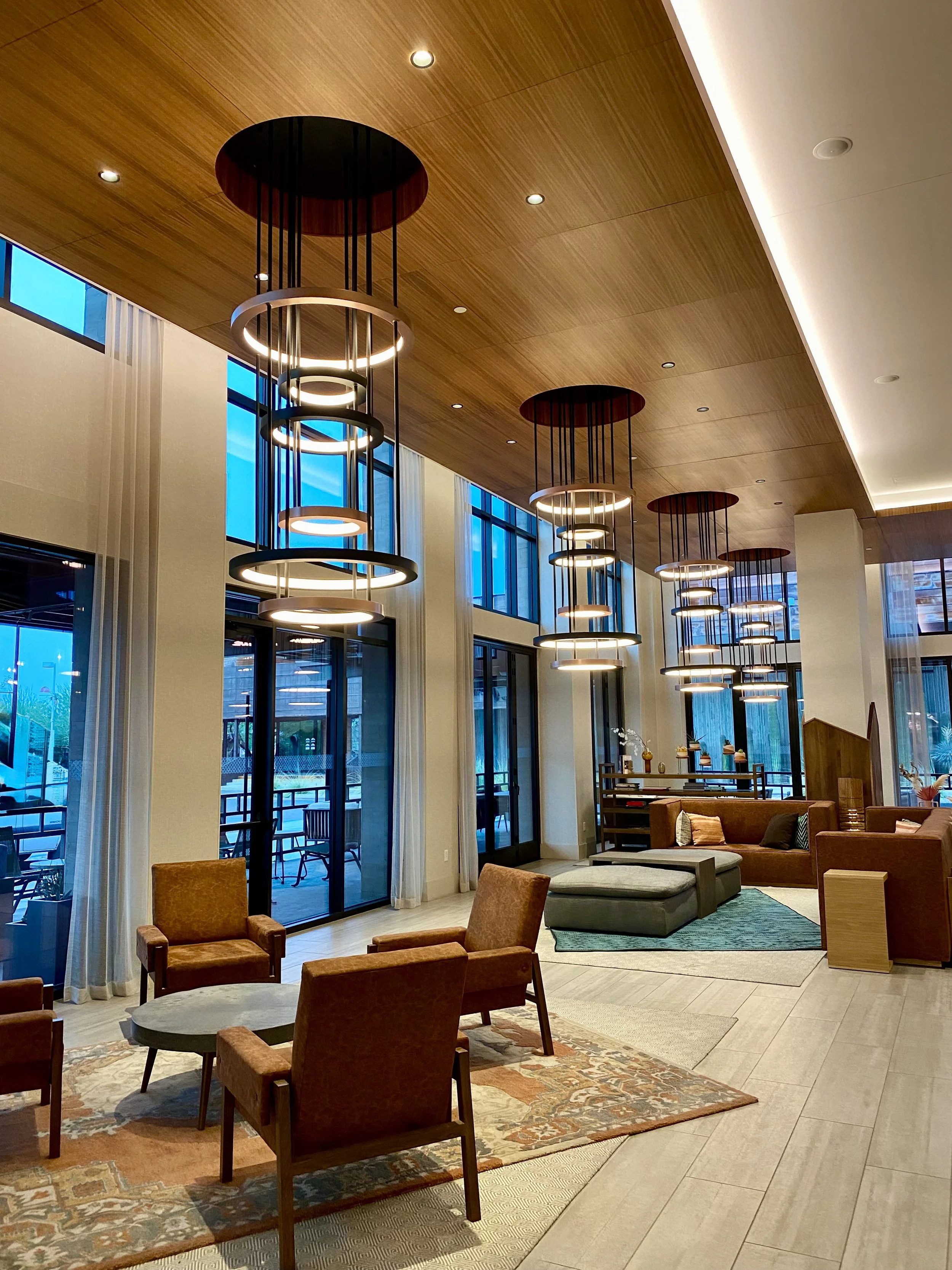 Interior of a modern, stylish lounge area with large windows, pendant lighting, chairs, sofas, and decorative elements.