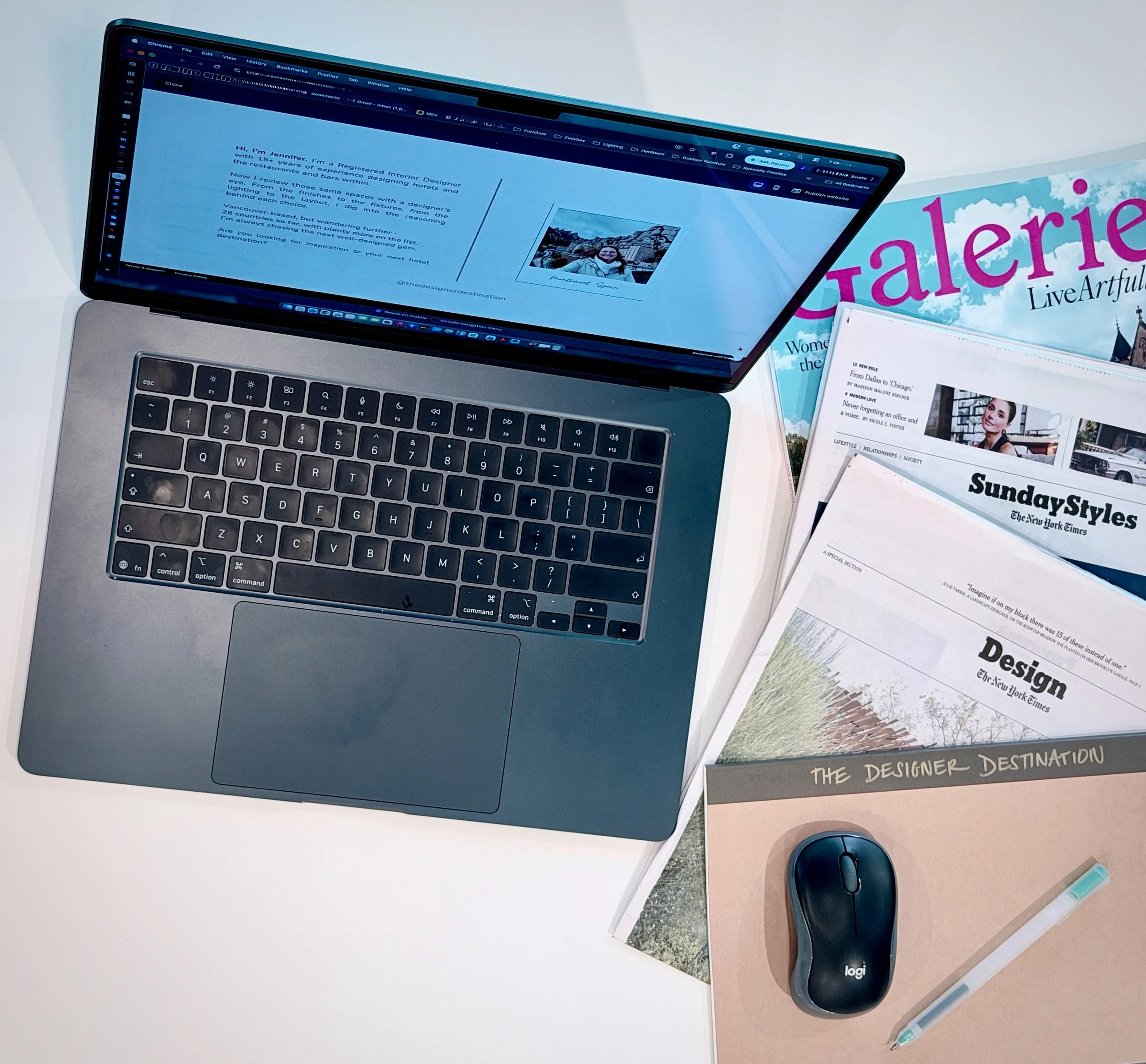 Open laptop displaying a webpage with a personal introduction and a photo of a woman near a mountain landscape; nearby are magazines titled 'tarierre' and 'SundaysStyles,' a computer mouse, two pens, and various office supplies on a white desk.