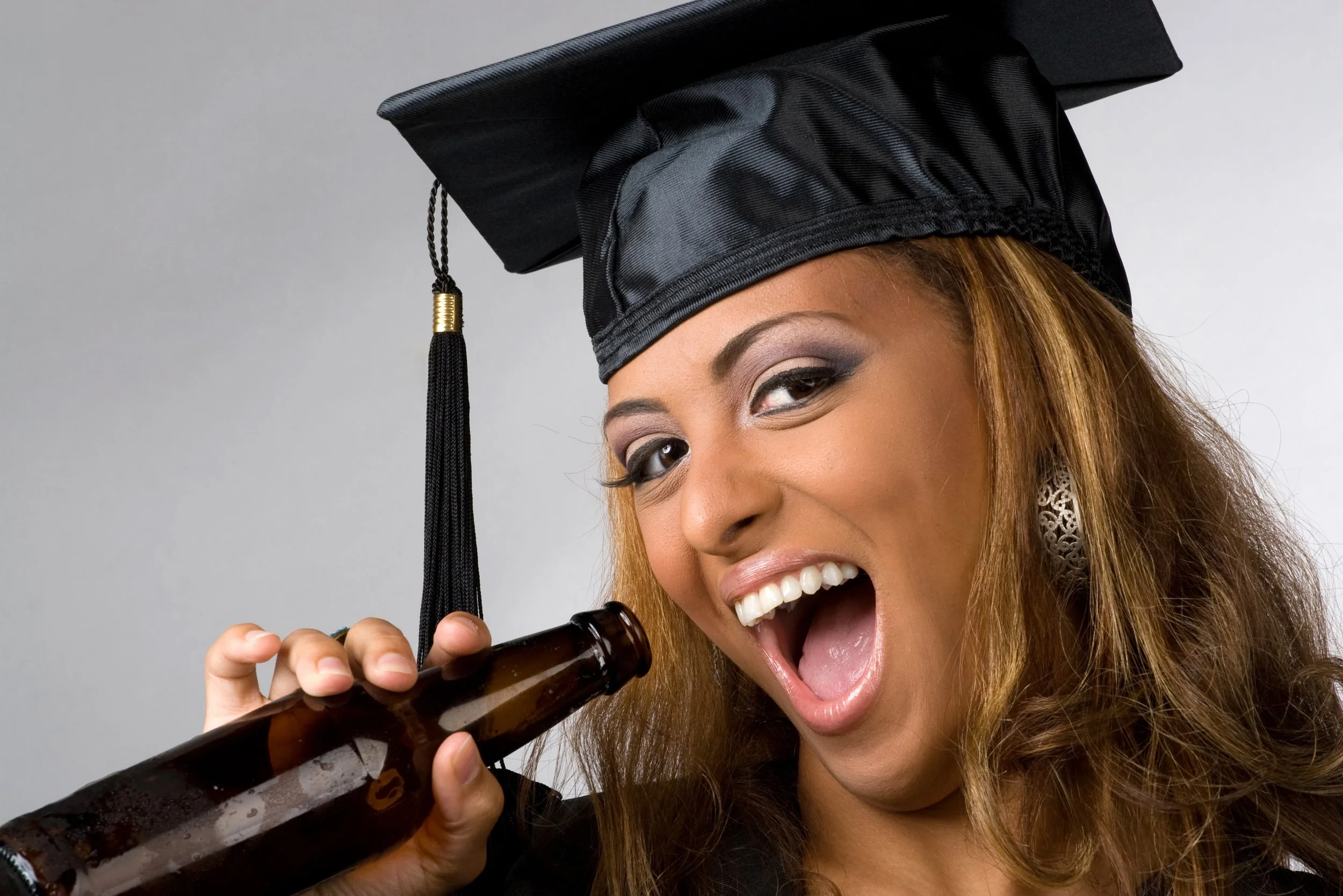 a-recent-graduate-posing-in-her-cap-and-gown-holding-beer-bottle-isolated-over-a-silve-SBI-301049308.jpg