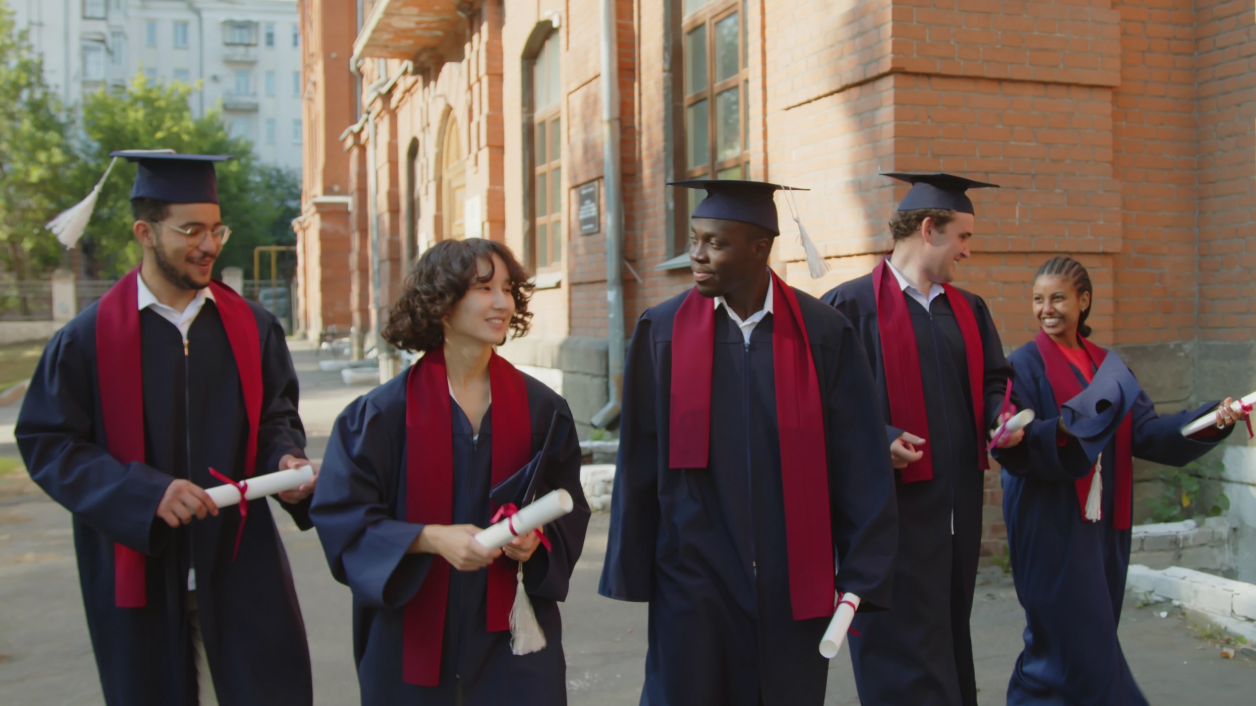 medium-long-tracking-shot-of-diverse-team-of-graduated-students-in-gowns-and-hats-comm-SBI-351050677.jpg