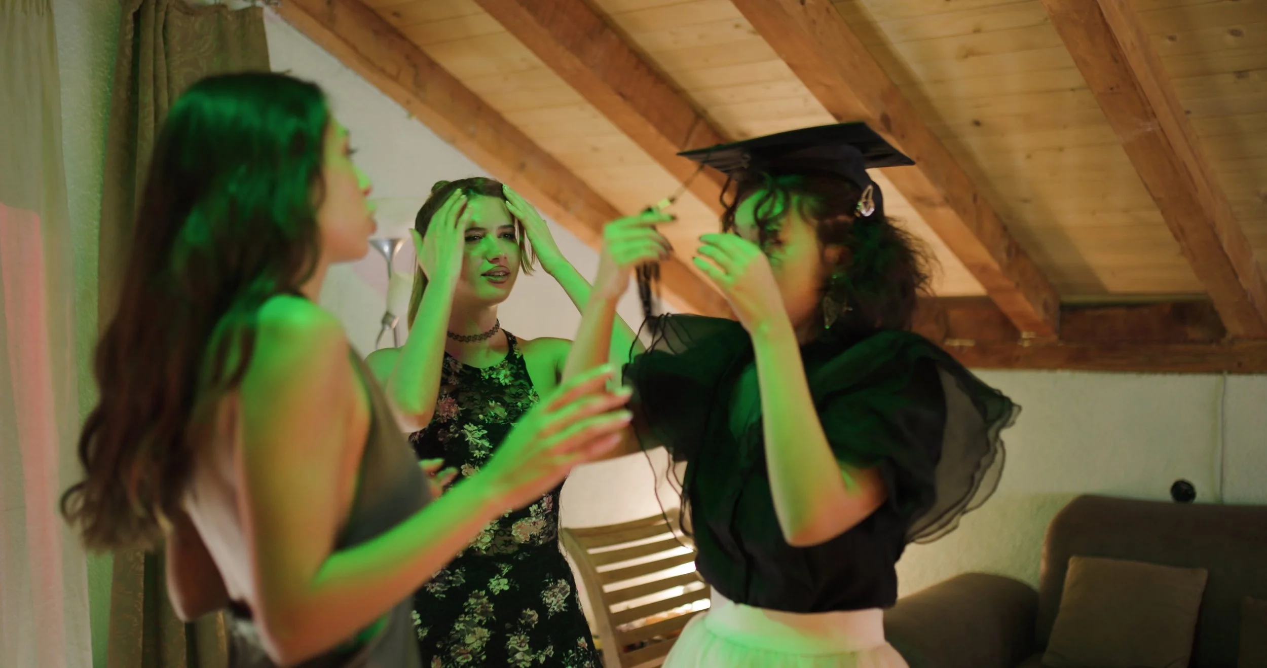 three-young-women-celebrate-graduation-at-home-a-friend-places-the-graduation-cap-on-t-SBI-357233667.jpg