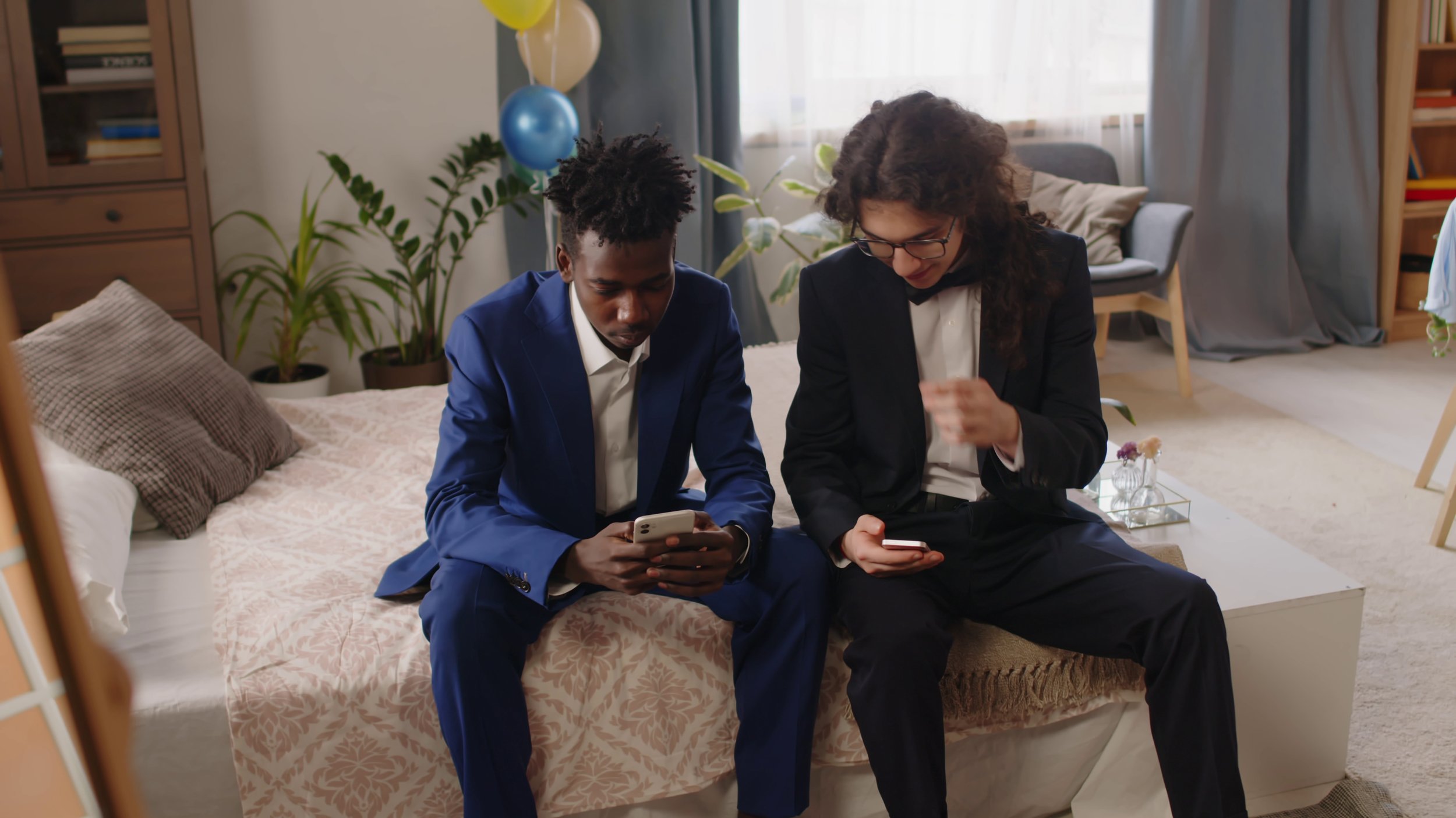 two-youthful-buddies-in-classy-suits-sitting-on-double-bed-in-domestic-room-and-discus-SBI-357584638.jpg