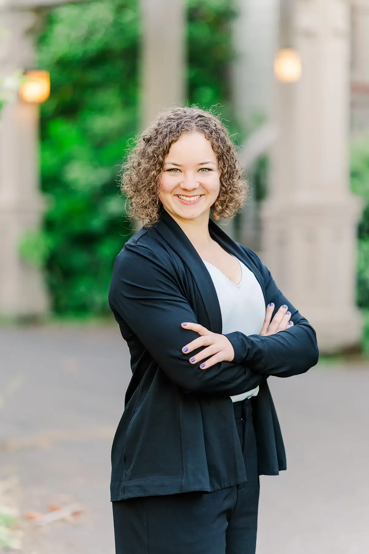 Smiling woman with curly hair standing outdoors with her arms crossed