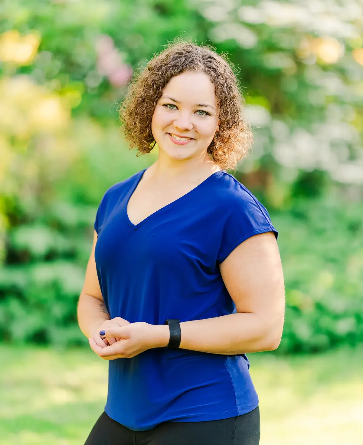 Smiling woman with curly hair wearing a blue shirt and fitness tracker outdoors