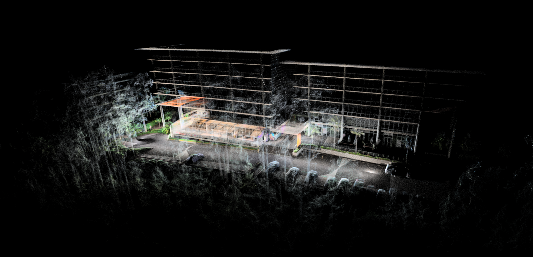 Nighttime aerial view of multi-story buildings under construction with exposed framework, surrounded by a parking lot with cars and illuminated by streetlights.