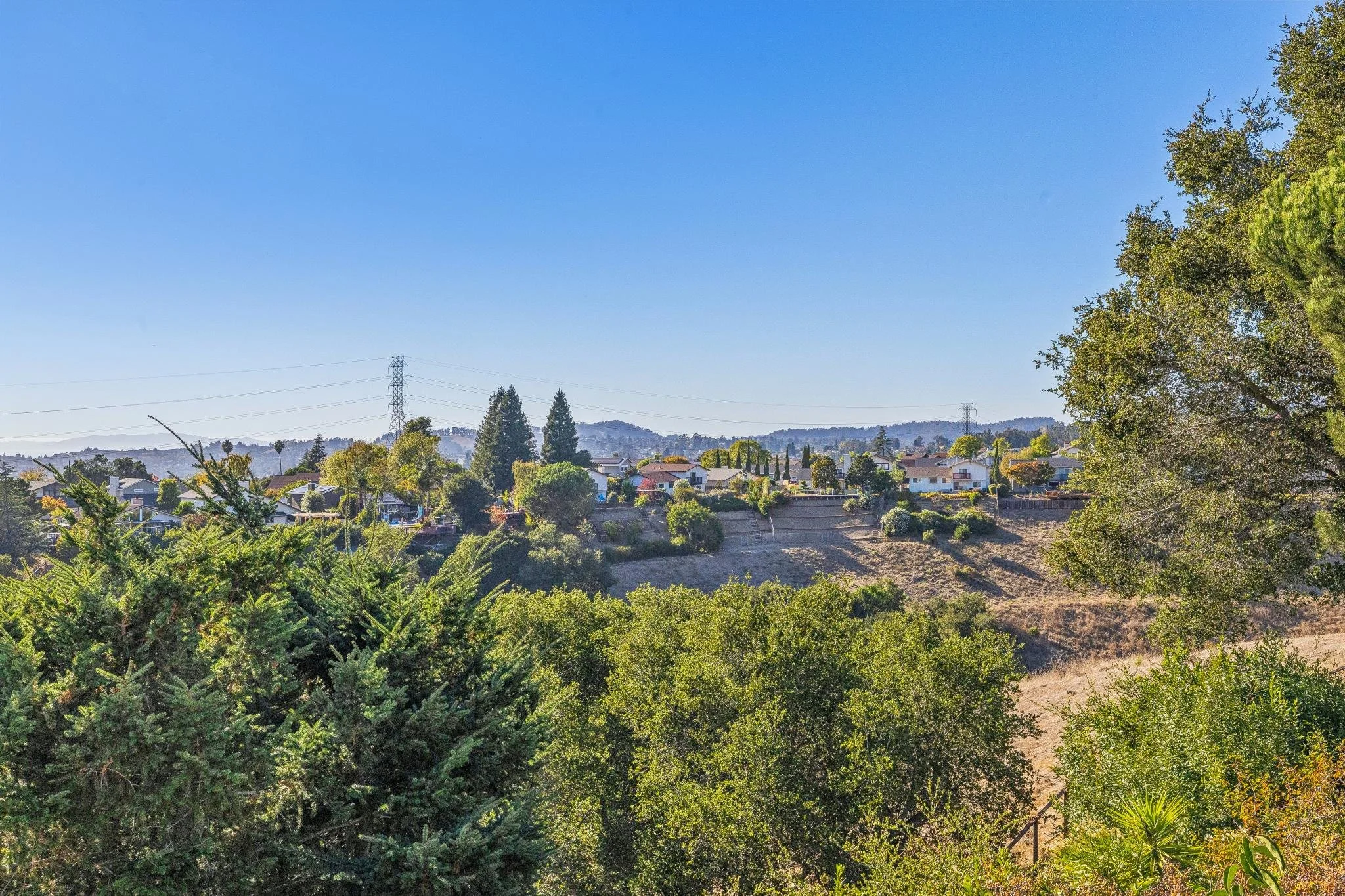 A suburban neighborhood with single-family houses, trees, and power lines under a clear blue sky.