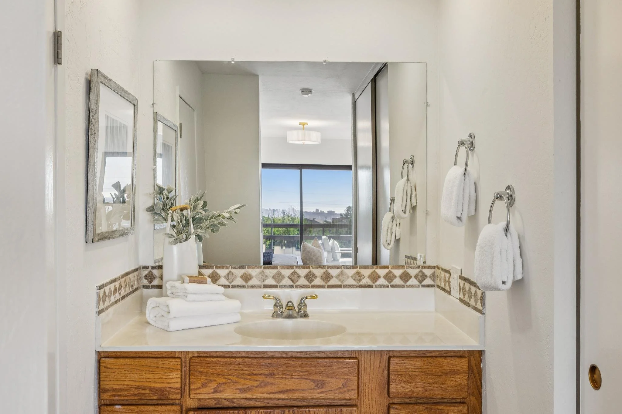 Bathroom vanity with a large mirror, towels, and a window showing a view of the outdoors.