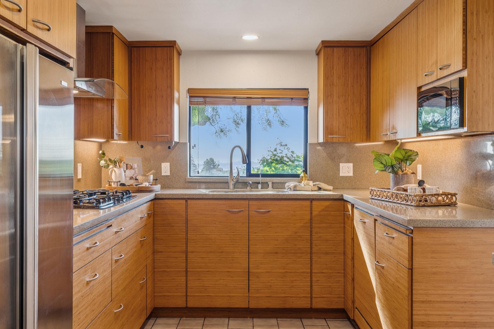 Kitchen with wooden cabinets, a window with blinds, and a countertop with plants and household items.