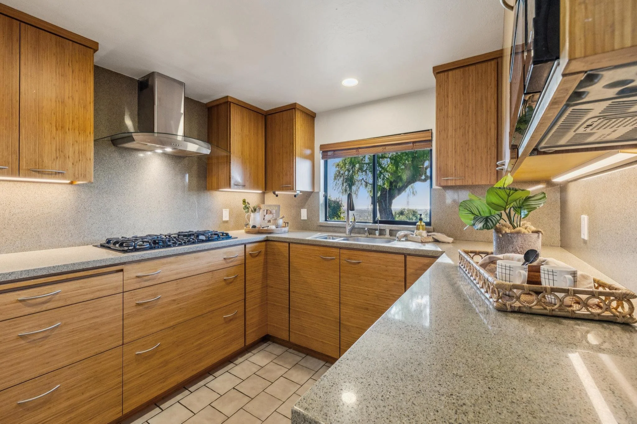 Kitchen with wooden cabinets, a window overlooking a tree, a potted plant, and a green speckled countertop with a basket and dishes.