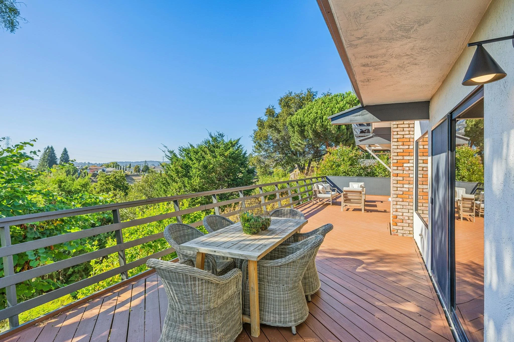 Outdoor balcony with a dining table and chairs, overlooking trees and a clear blue sky.