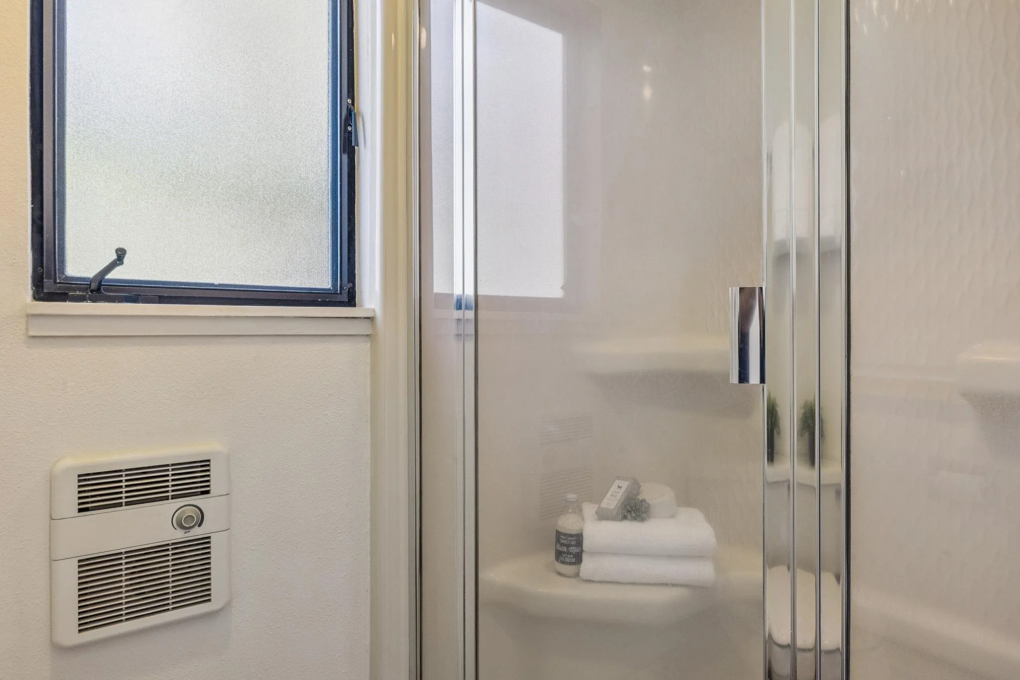 View of a bathroom shower with glass door, a small window with frosted glass, and a wall-mounted vent.