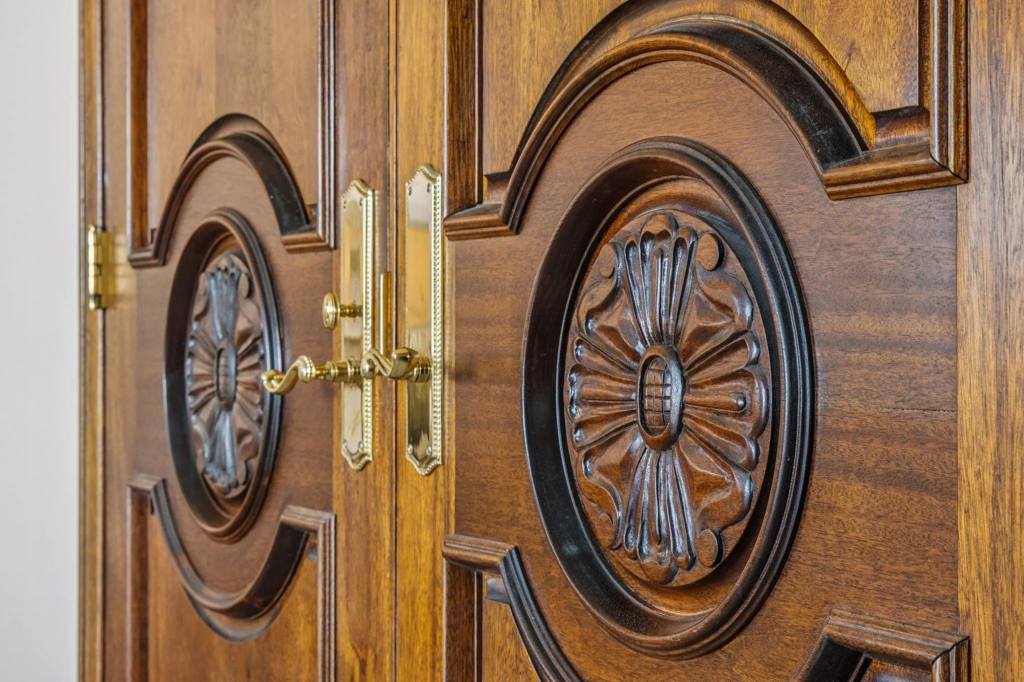 Close-up of a polished wooden table with ornate carved circular designs and brass handles.