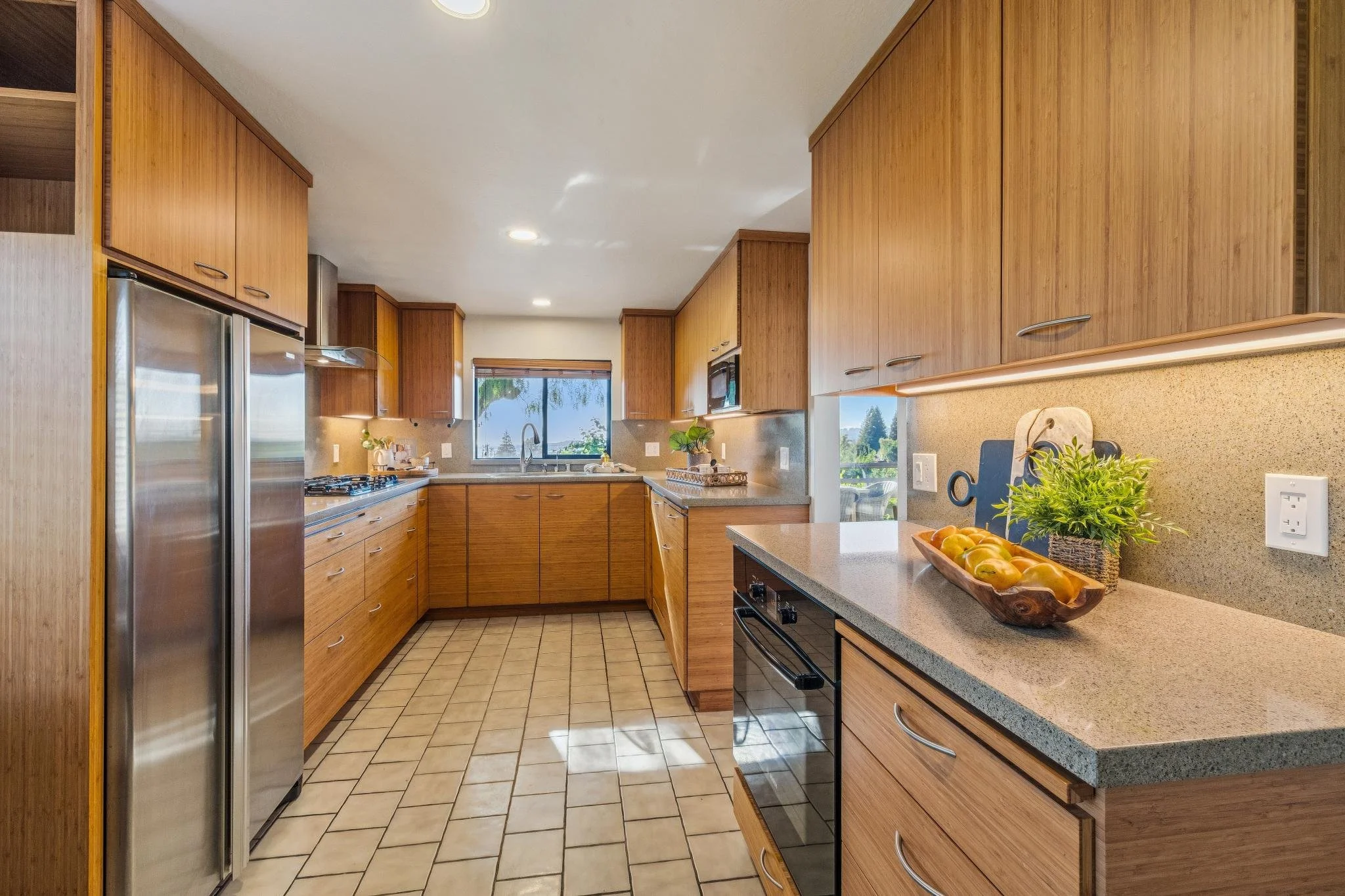 A kitchen with wooden cabinets, a window, a countertop with a fruit tray, potted plants, and stainless steel appliances.