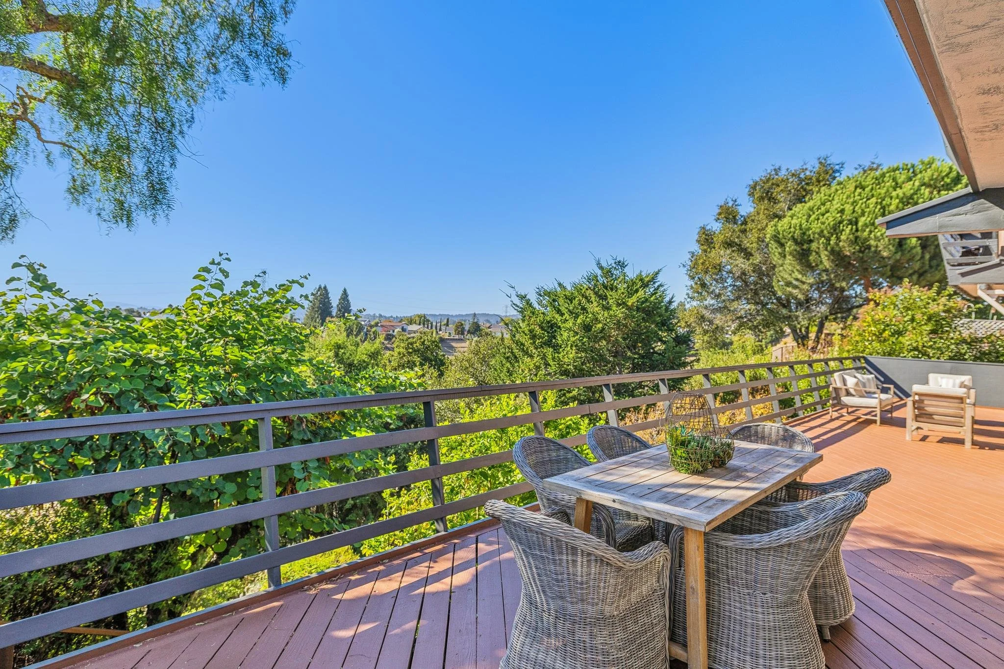 View of a backyard deck with outdoor furniture and lush green trees under a clear blue sky.