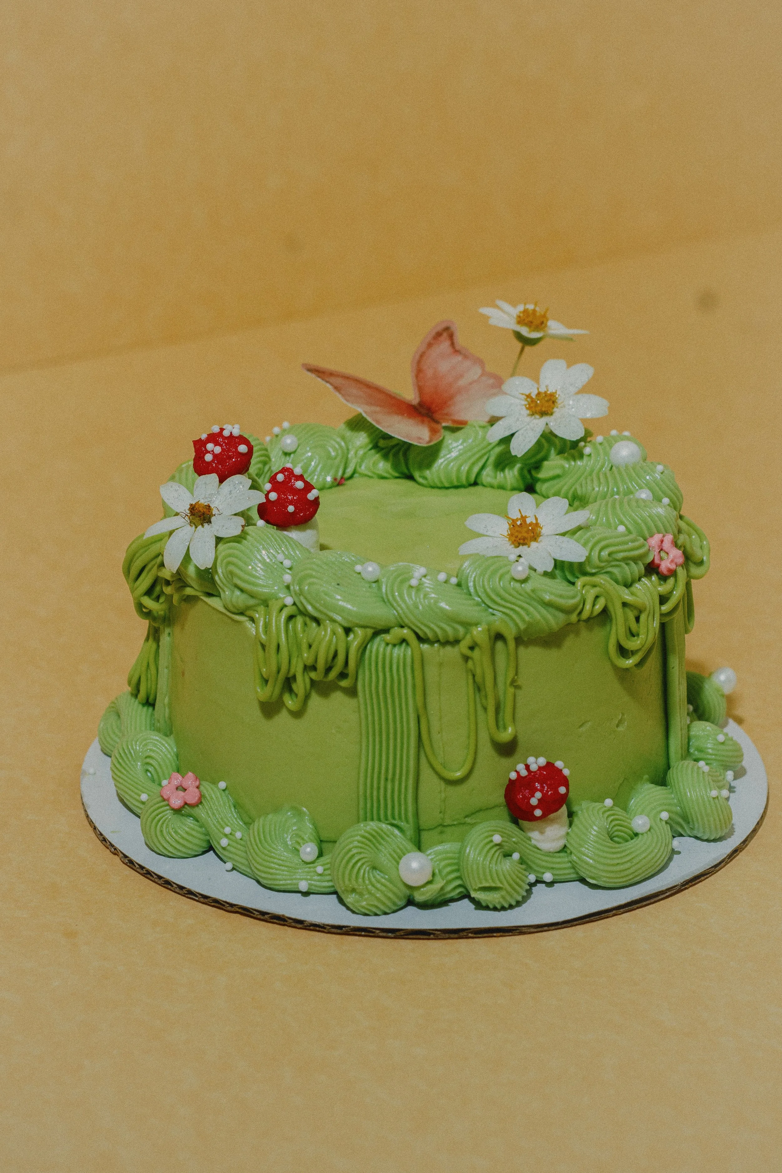 A green forest pixi cake decorated with white flowers, red mushrooms, and a butterfly topper. Bastrop, Texas