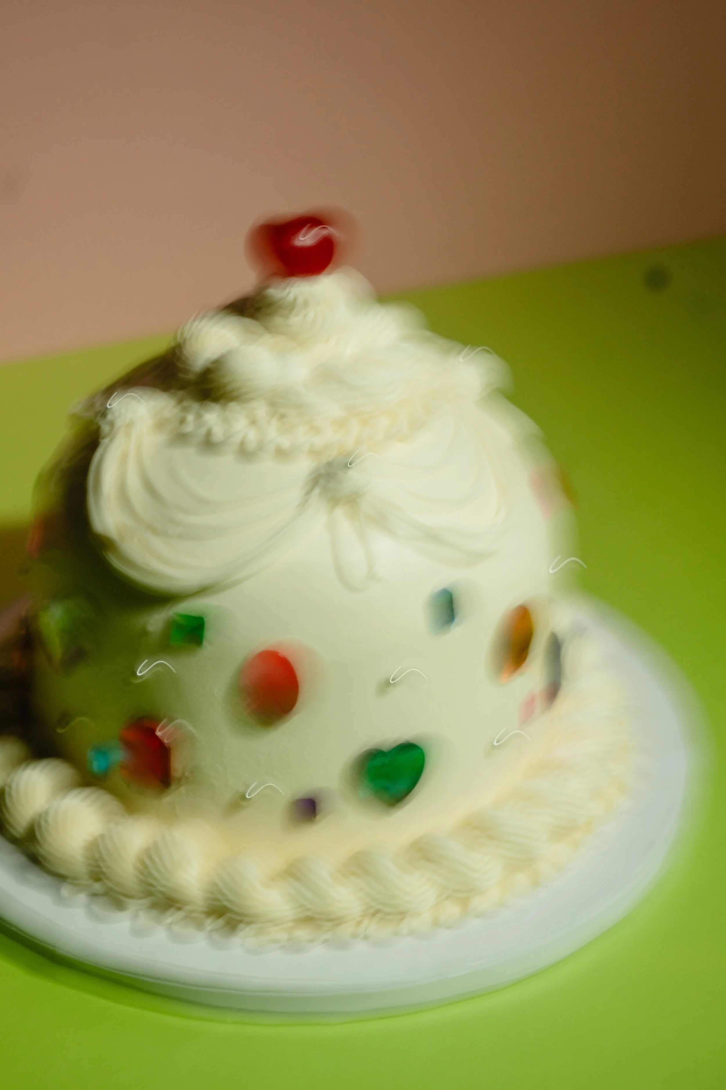 A colorful cake with various round candies and sprinkles, topped with a cherry.