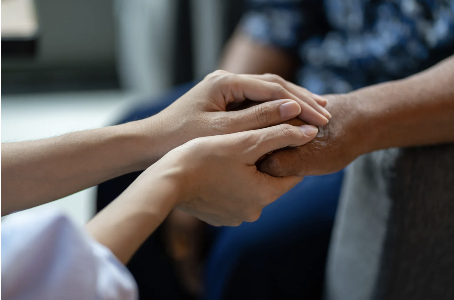 A person gently holding and comforting an elderly person's hand.