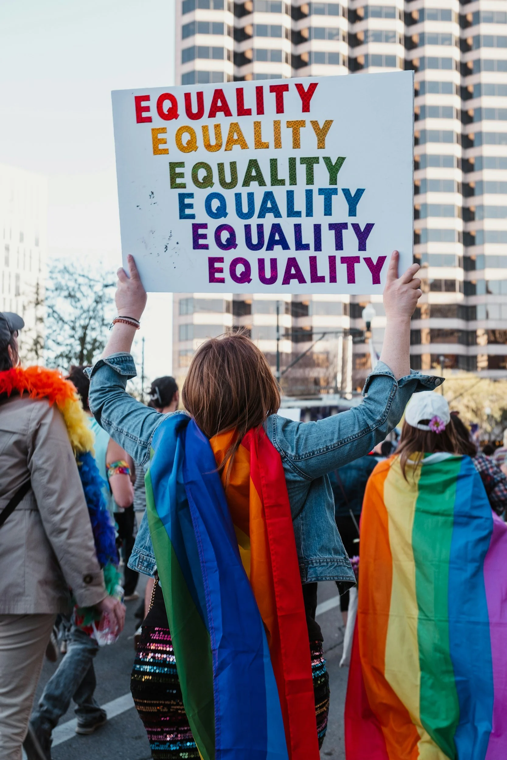 Pride parade participants holding a colorful “Equality” sign and rainbow flags in a city street