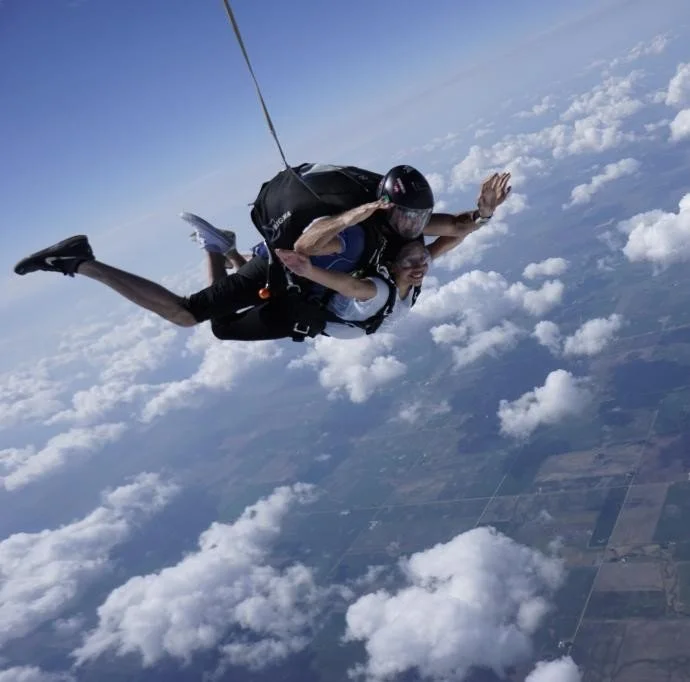 Tandem skydivers free-falling above clouds and farmland