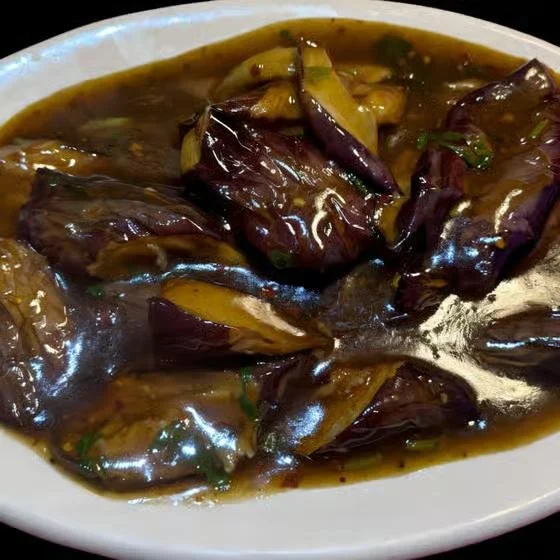 Eggplants in a dark, savory sauce served in a white oval dish.