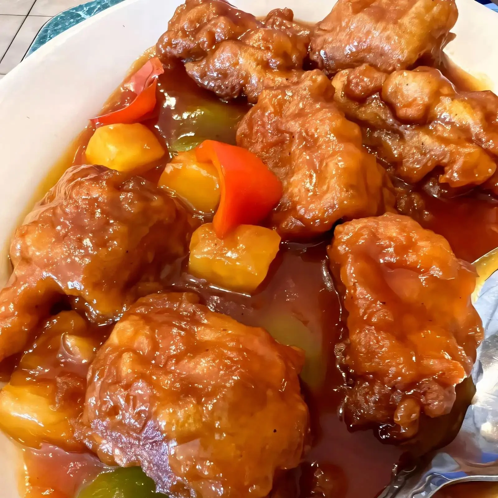 A plate of sweet and sour chicken with rice, featuring crispy chicken pieces, bright red and yellow bell peppers, pineapple chunks, and a glossy sauce.