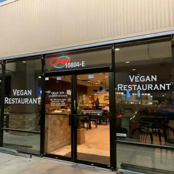 Front view of a vegan restaurant with glass doors and windows, displaying 'Vegan Restaurant' signs, an open sign, and the interior with tables and customers.