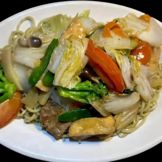 Stir-fried noodles with vegetables including broccoli, carrots, and mushrooms on a white plate.