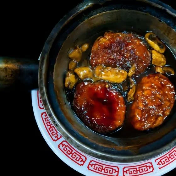 Three fried hamburgers in a skillet with mushroom slices and sauce, on a decorative plate.
