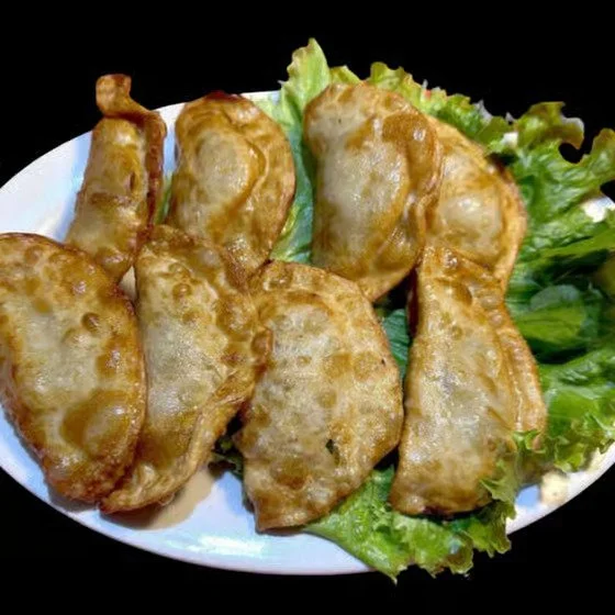 Seven golden fried spring rolls on a white plate with green lettuce leaves in the background.