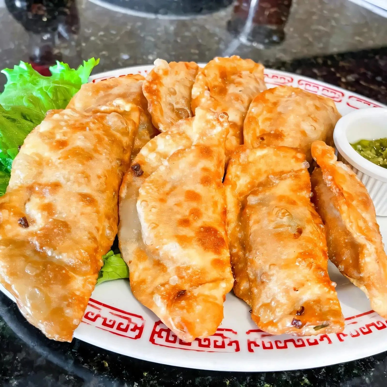 Close-up of several cooked chicken drumsticks covered in orange sauce, served on a decorative plate with a side of green sliced jalapenos in a small white cup and green lettuce leaves.
