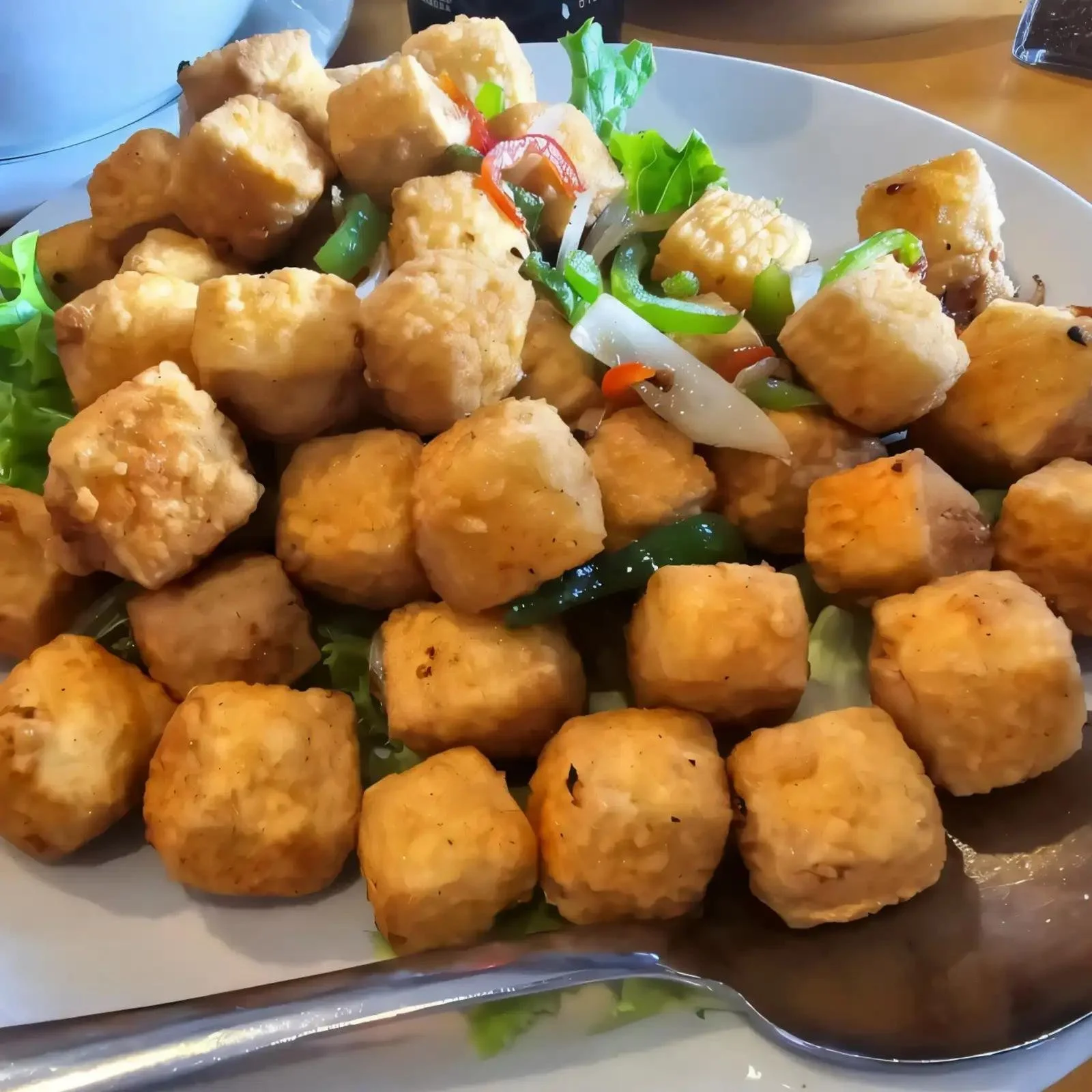 A plate of fried tofu cubes garnished with sliced bell peppers, onions, and lettuce.