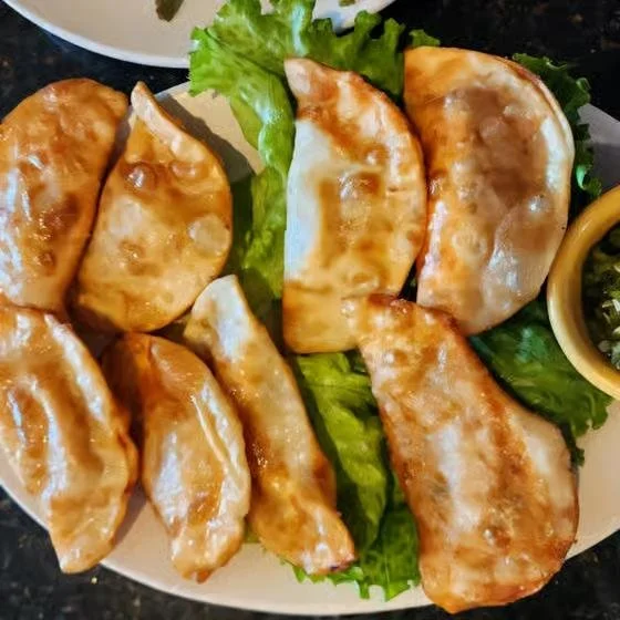 Plate of six fried dumplings with lettuce and dipping sauce on the side, served on a white plate.
