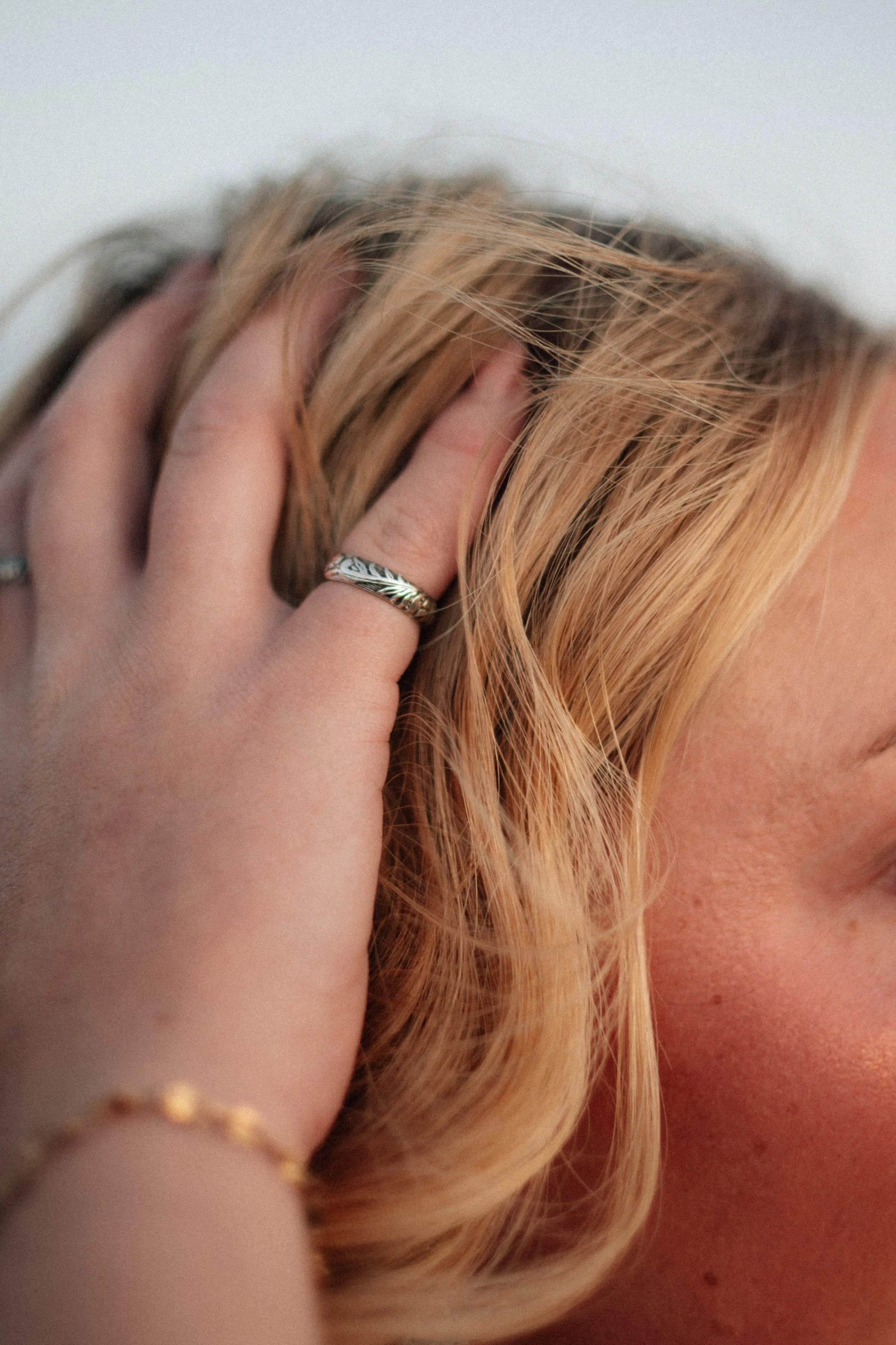Close-up of a person with blonde hair touching their head, with a focus on the hair and hand wearing a silver ring. Wearing the Ranch Hand Silver ring, an engraved ring made by ponderosa silver.