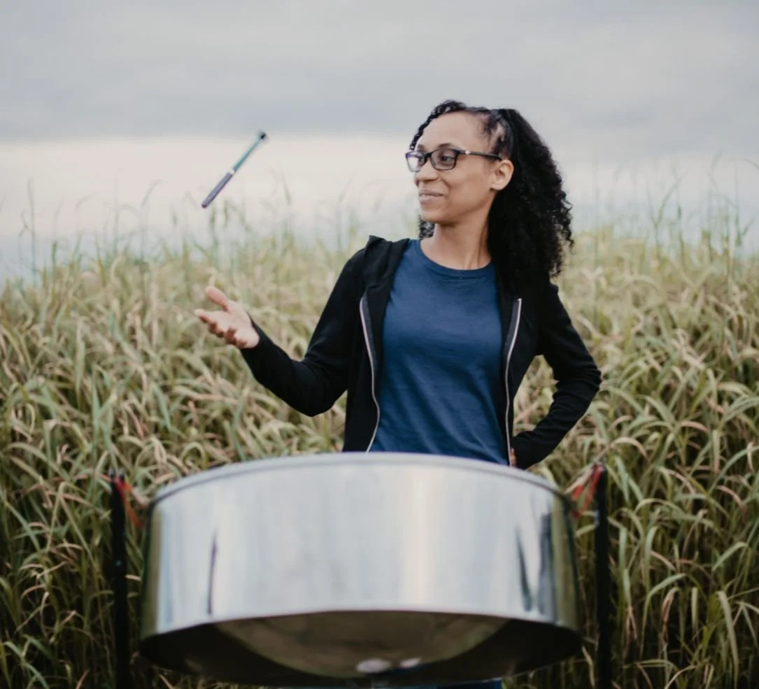 Miriyam Wilson flipping sticks and posing behind a Steelpan.
