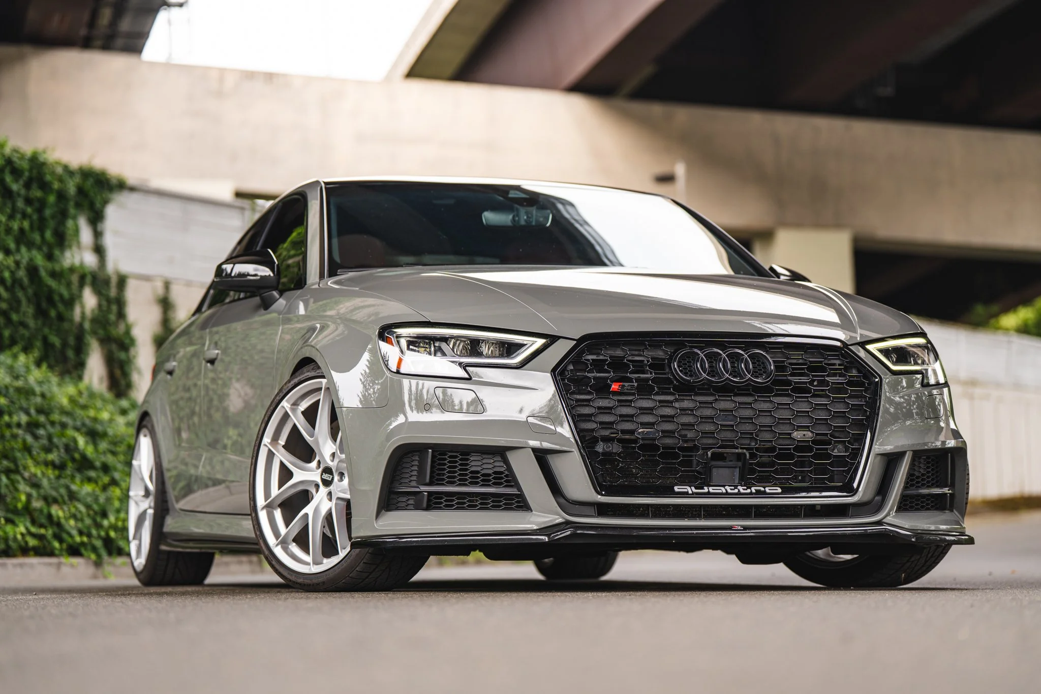 A silver Audi S4 Quattro sports car parked outdoors near a modern building with geometric architecture and greenery.