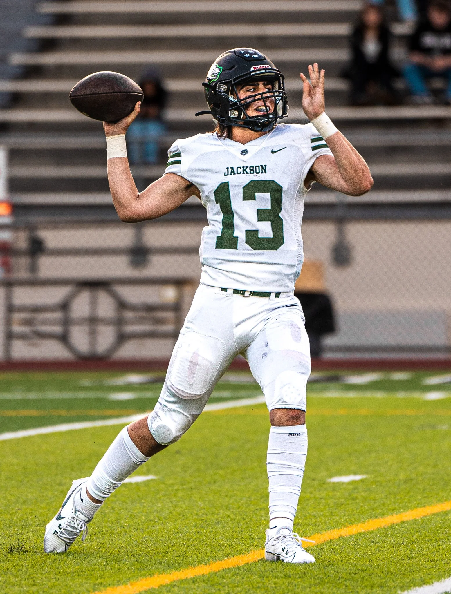 A football player in a white jersey with 'Jackson' and the number 13, and a black helmet, preparing to throw a football on a field with green grass and yellow yard lines.