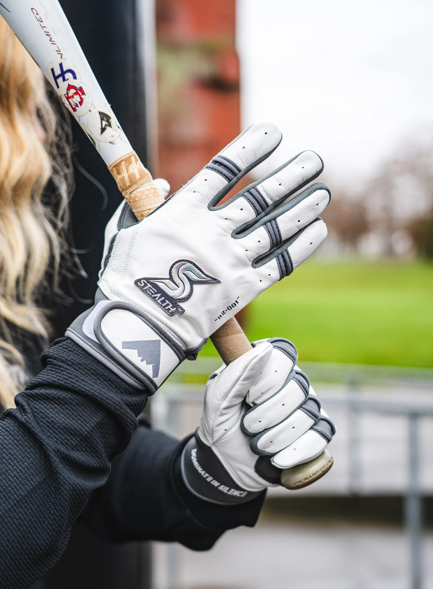 Close-up of a person's gloved hands gripping a golf club, with a golf course and a brick wall in the background.