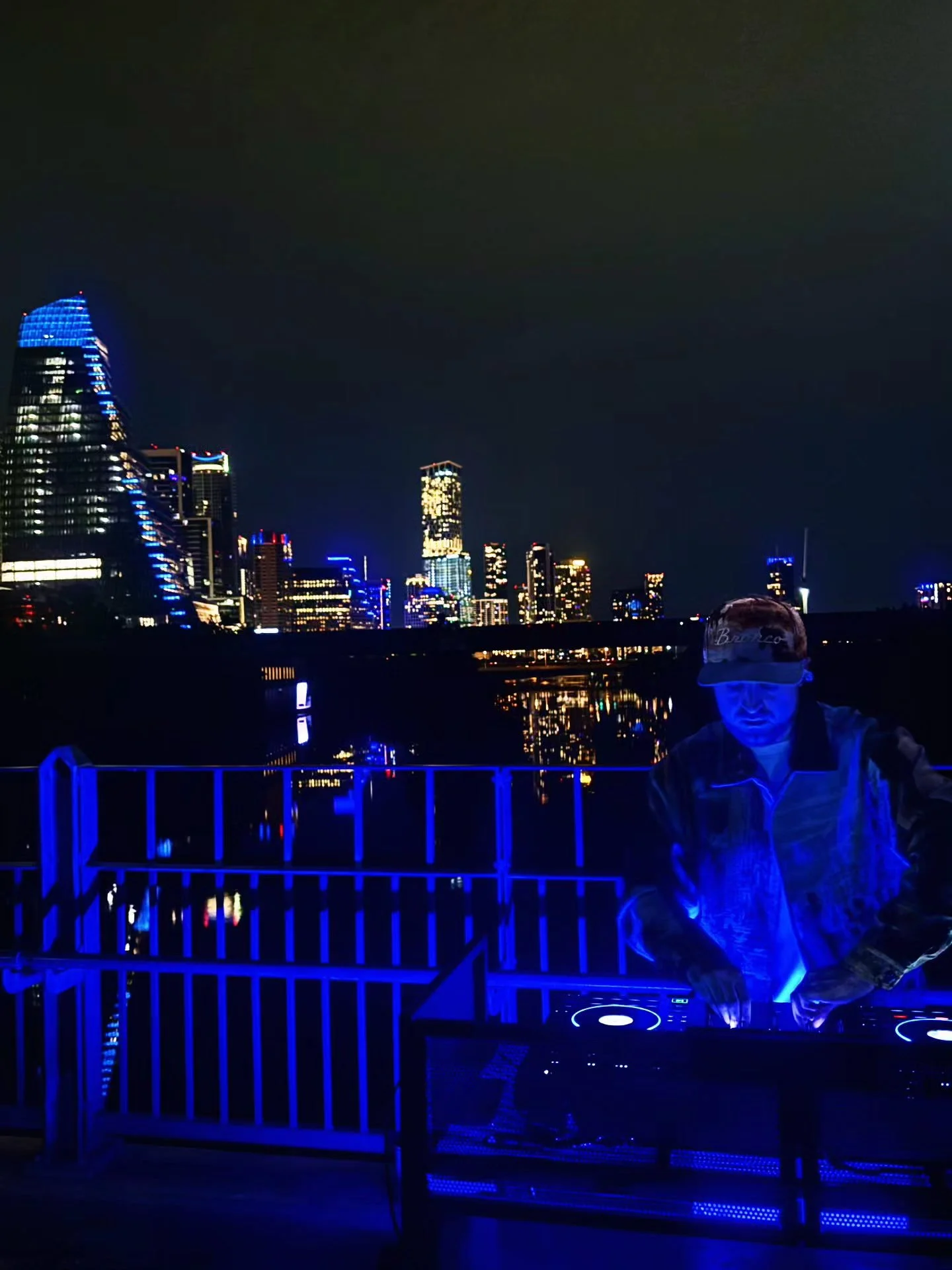 DJ Sona performing against the Austin city skyline at night.