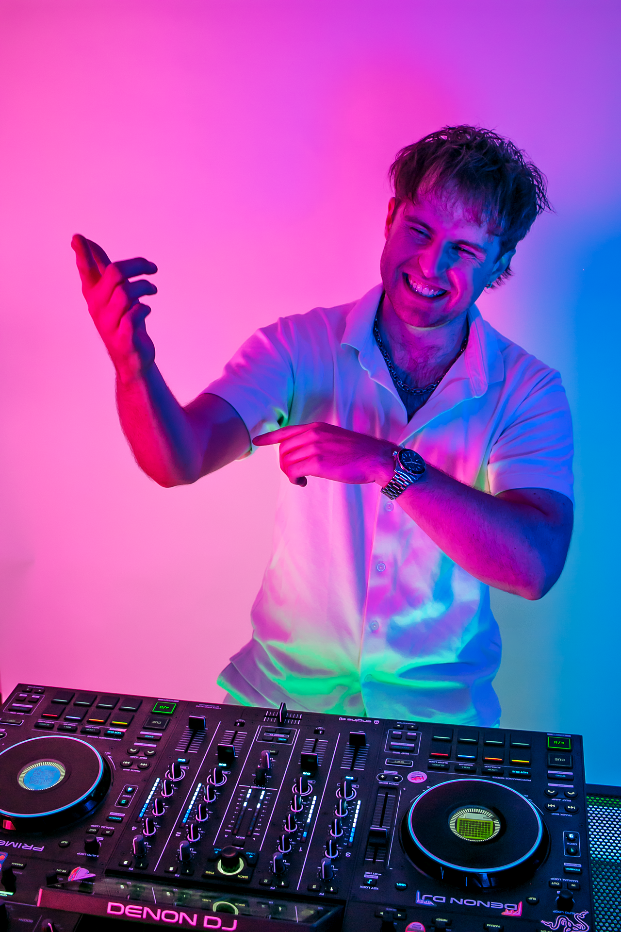 DJ Sona smiling and pointing at a DJ controller in front of him, illuminated by colorful neon lights.