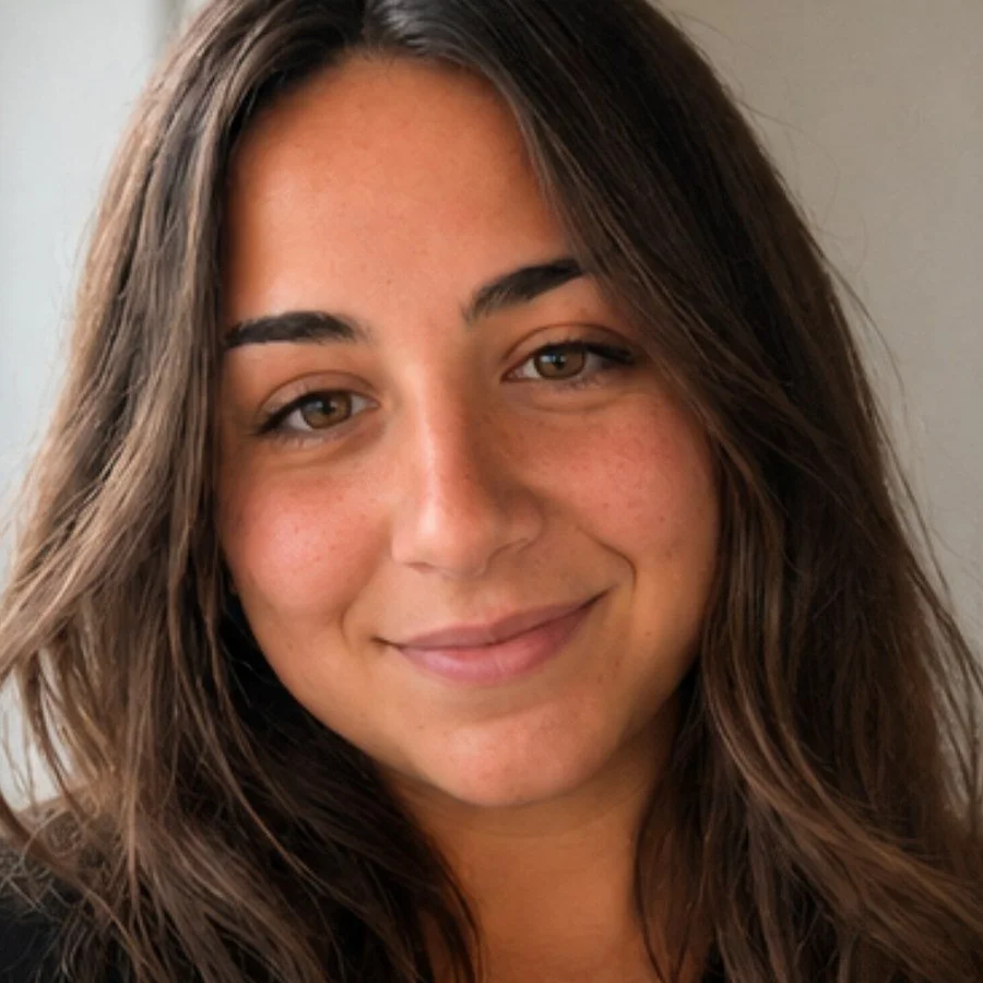 Close-up of a young woman with long, wavy brown hair and light brown eyes, smiling softly at the camera.