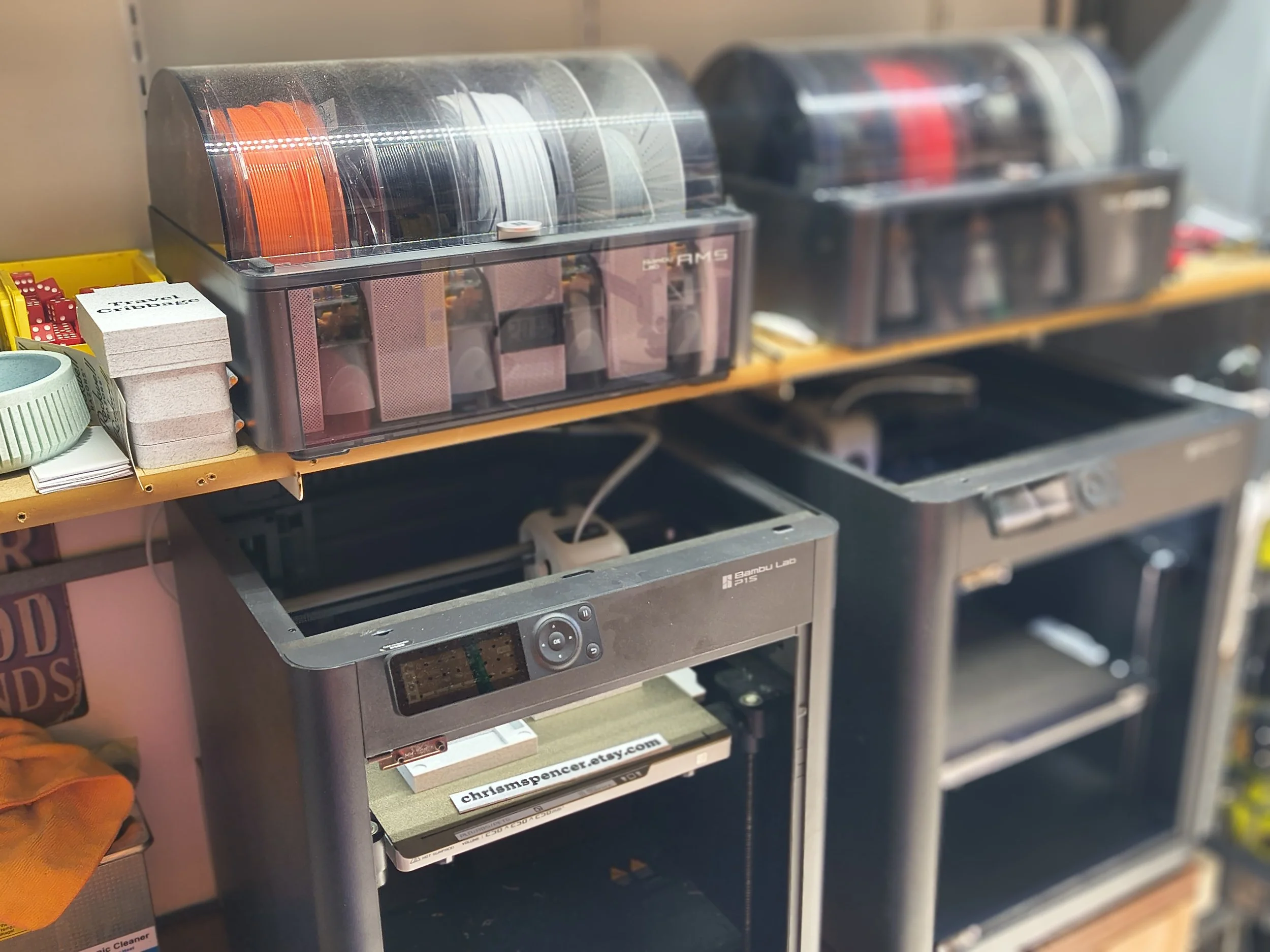 A couple of the Bambu P1S printers with AMS units and filament I use in my print farm.