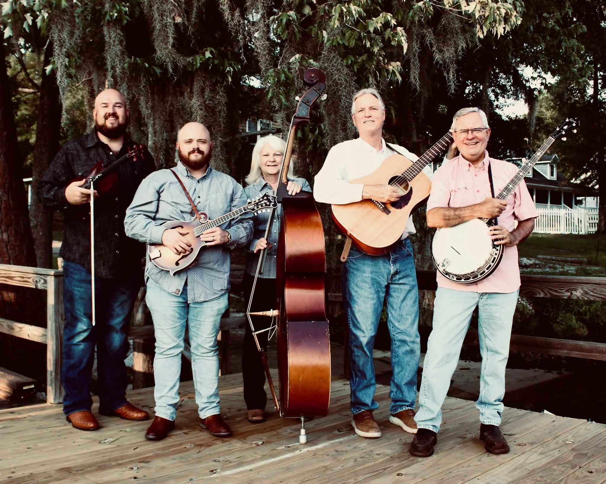 Wire & Wood bluegrass band posing outdoors with their instruments beneath a tree.