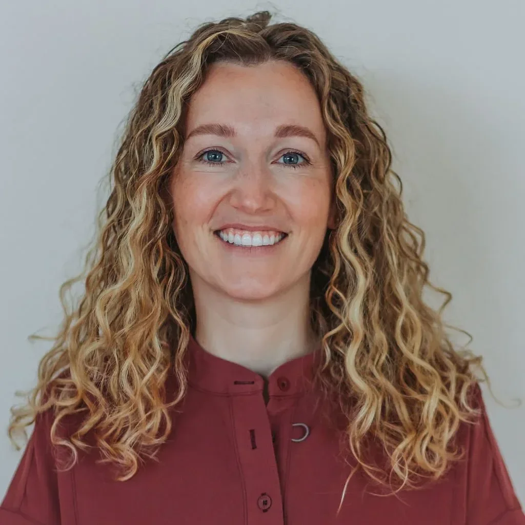 Dr. Angela Koenig with curly red hair smiling against a plain white background.