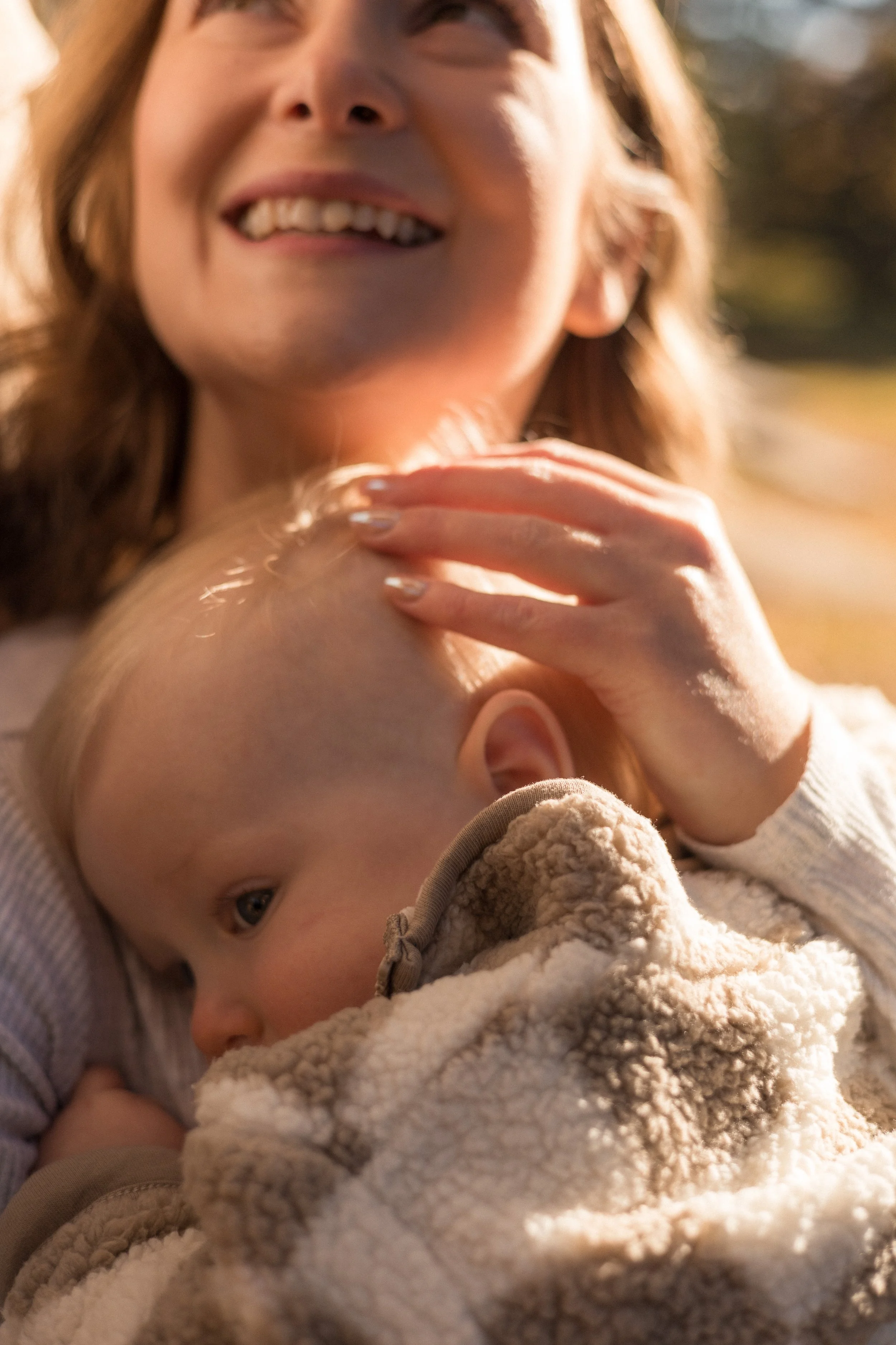 A woman smiling and looking at a young child lying in a cozy blanket, with the child gazing up.