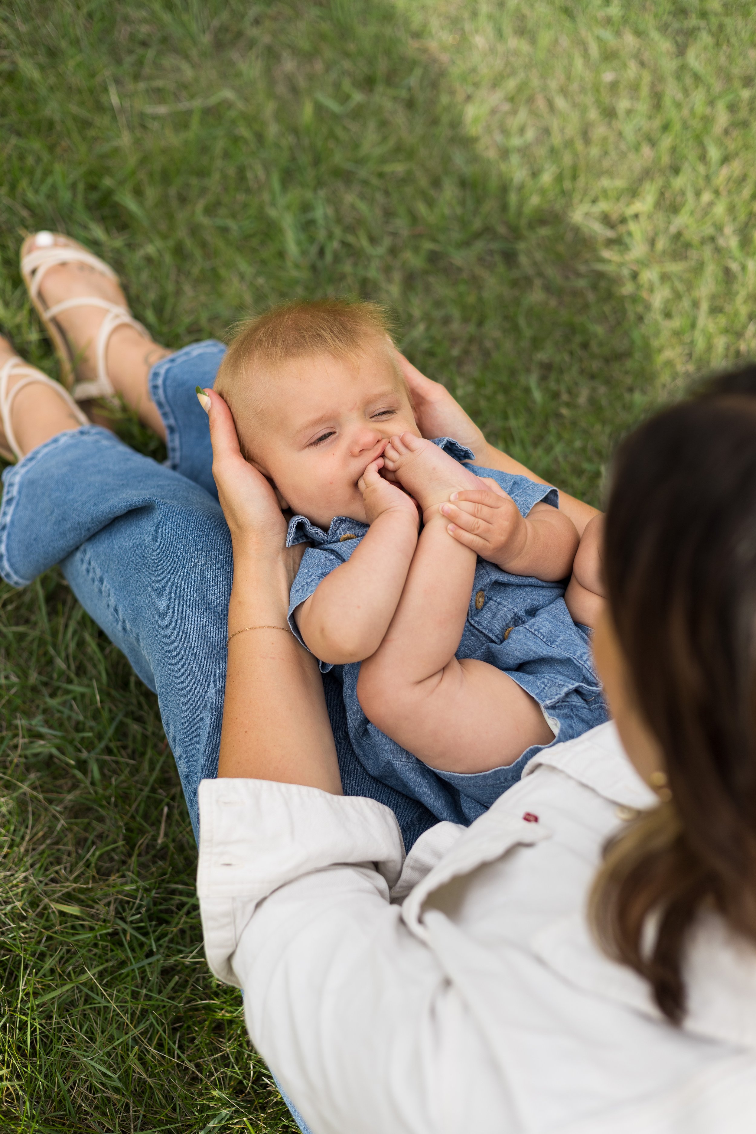 A woman lying on grass holding a young child's head and embracing them, with a background of green grass.
