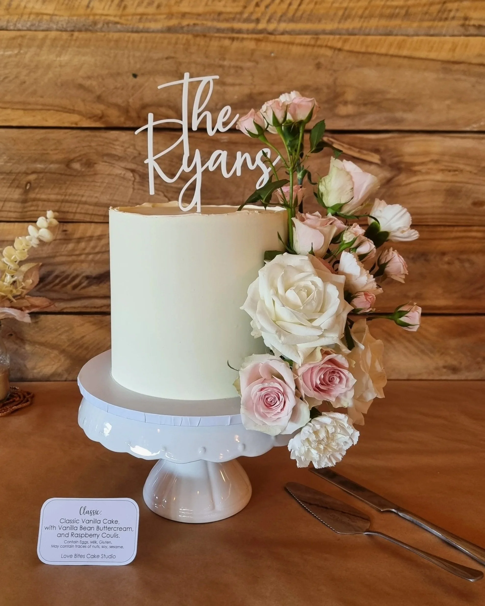 Smooth white wedding cake with an abundance of white and pink roses down one side.