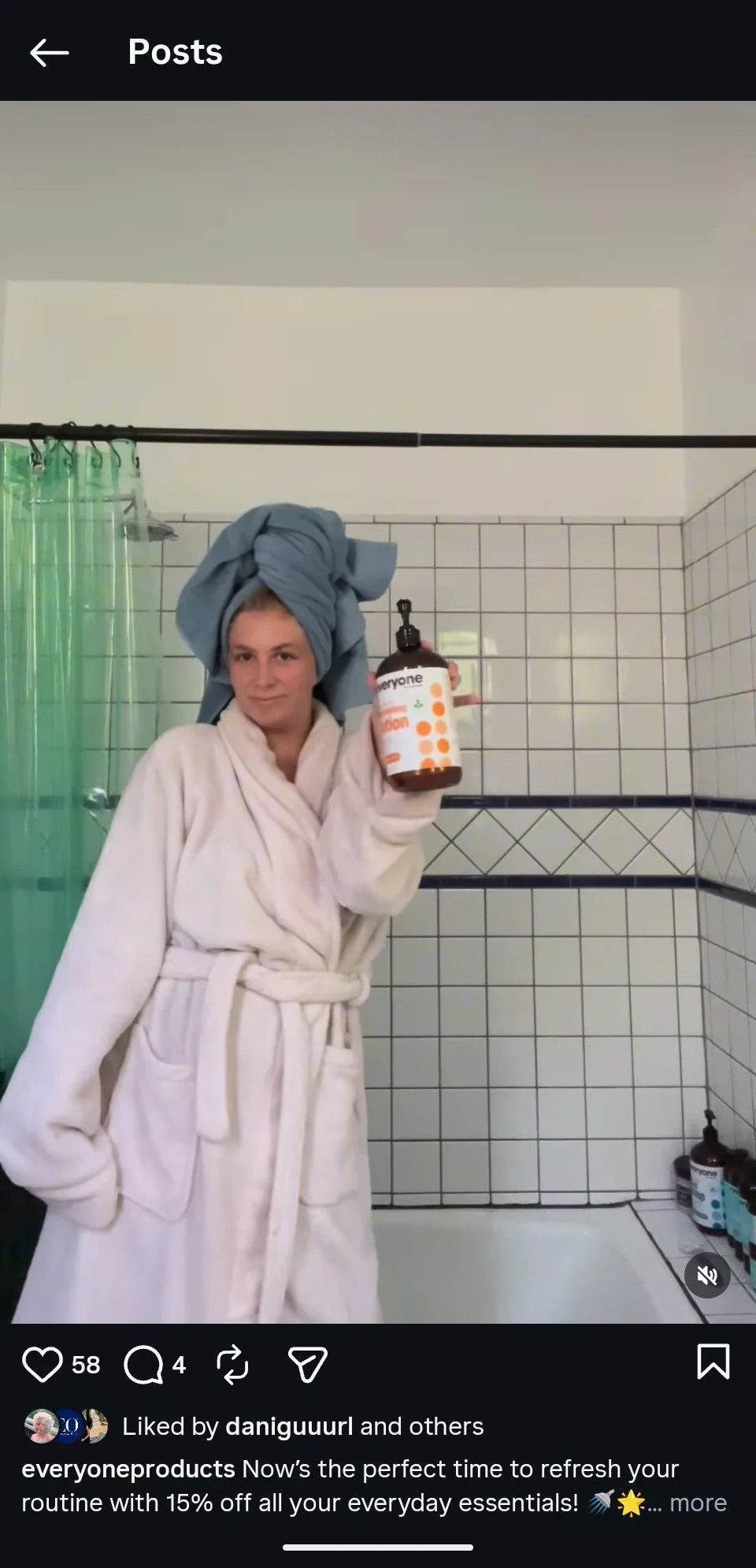 Woman wearing a bathrobe and towel on head, holding a bottle of Everyone hand soap in a bathroom with tiled walls and a shower curtain.