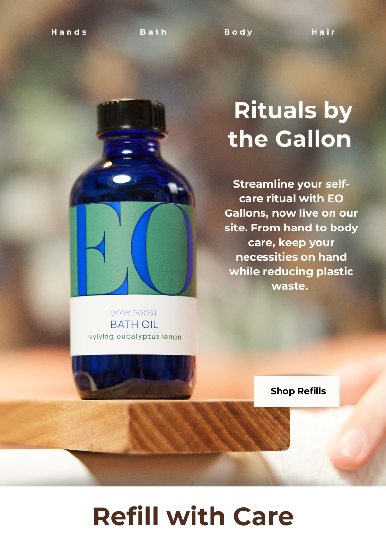 A blue bottle of EO Body Boost Bath Oil on a wooden surface with blurred background, promotional text about self-care rituals, and a button labeled 'Shop Refills'.