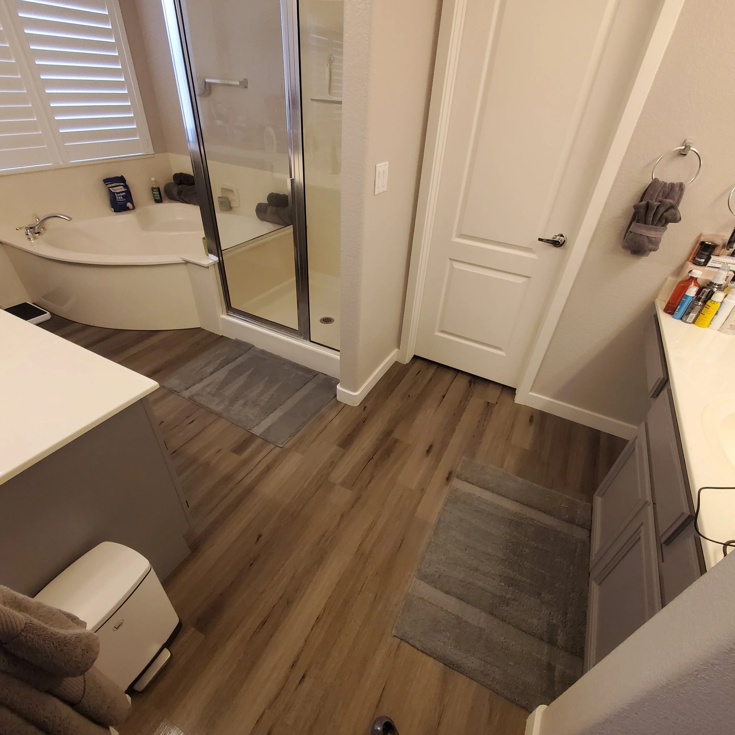A bathroom with a corner bathtub, a glass shower enclosure, a white door, a towel hanging on a towel ring, and various bathroom items on a counter.