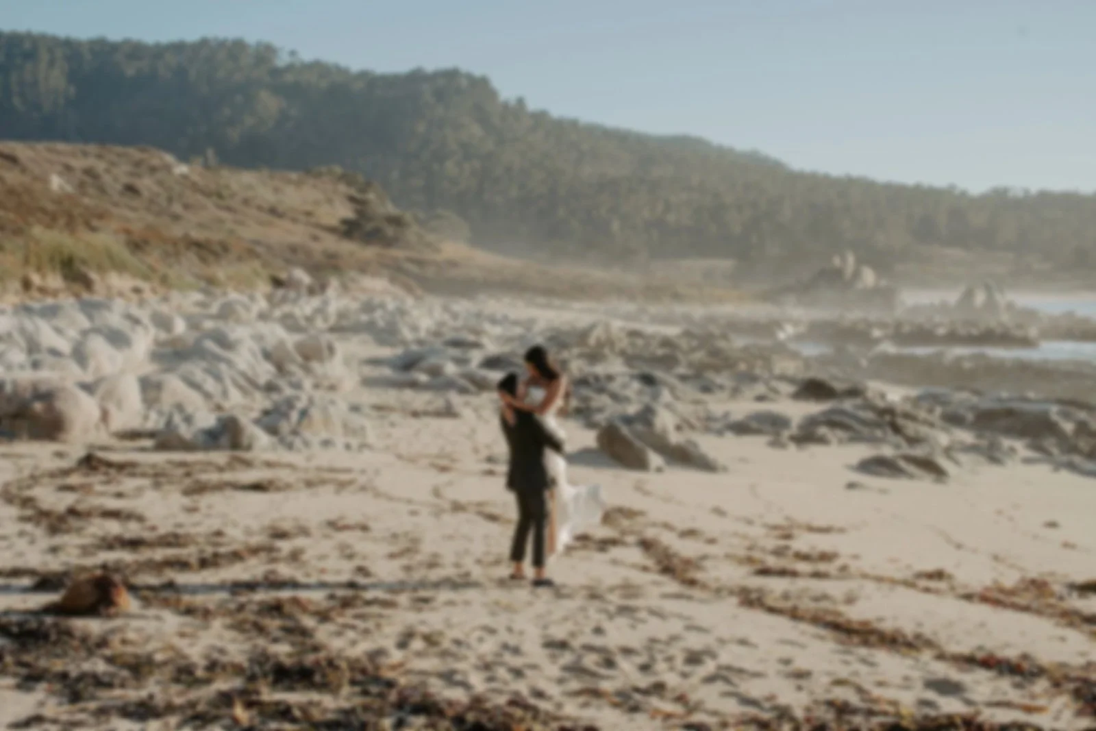 Couple on the beach embracing near rocks with ocean and hills in the background